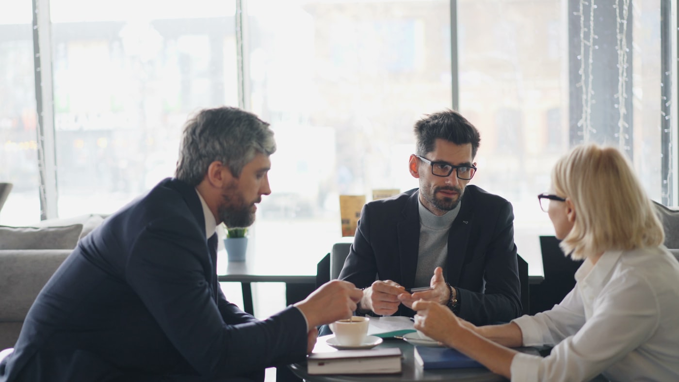 Three people in a focused professional conversation at a table.
